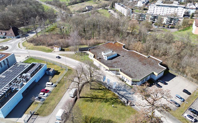 Luftaufnahme eines Gebäudekomplexes im Göppinger Stauferpark mit Flachdach, Parkplätzen und Grünfläche. Umgeben von Gewerbe- und Wohnobjekten.
