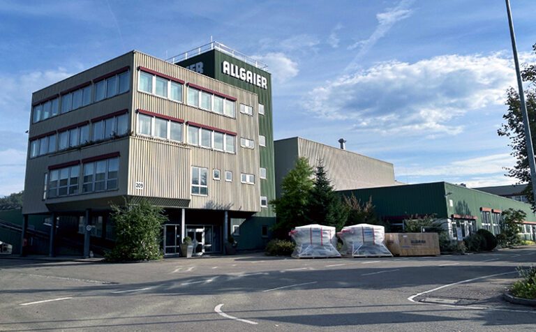 Großes Firmenareal mit Zufahrt im Vordergrund und mehreren Hallen im Hintergrund. Große Aufschrift "Allgaier". Die Fassade ist Grau und Dunkelgrün.