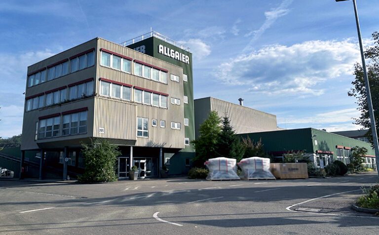 Großes Firmenareal mit Zufahrt im Vordergrund und mehreren Hallen im Hintergrund. Große Aufschrift "Allgaier". Die Fassade ist Grau und Dunkelgrün.