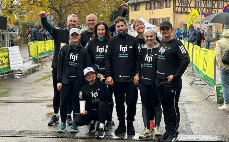 Gruppenbild des fgi-Teams im Ziel des Alb Marathons in Schwäbisch Gmünd. Das Team ist mit fgi-Laufshirts in Schwarz mit weißer und mintgrüner Aufschrift ausgestattet. Alle schauen in die Kamera. Im Hintergrund Banner des Alb Marathons.