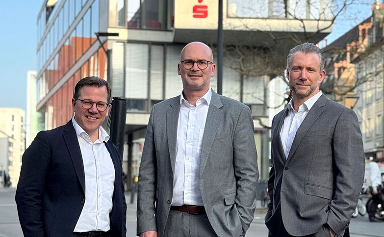 Drei Mitarbeiter von fgi in Businesskleidung vor einem Bürogebäude im Stadtzentrum von Ulm.